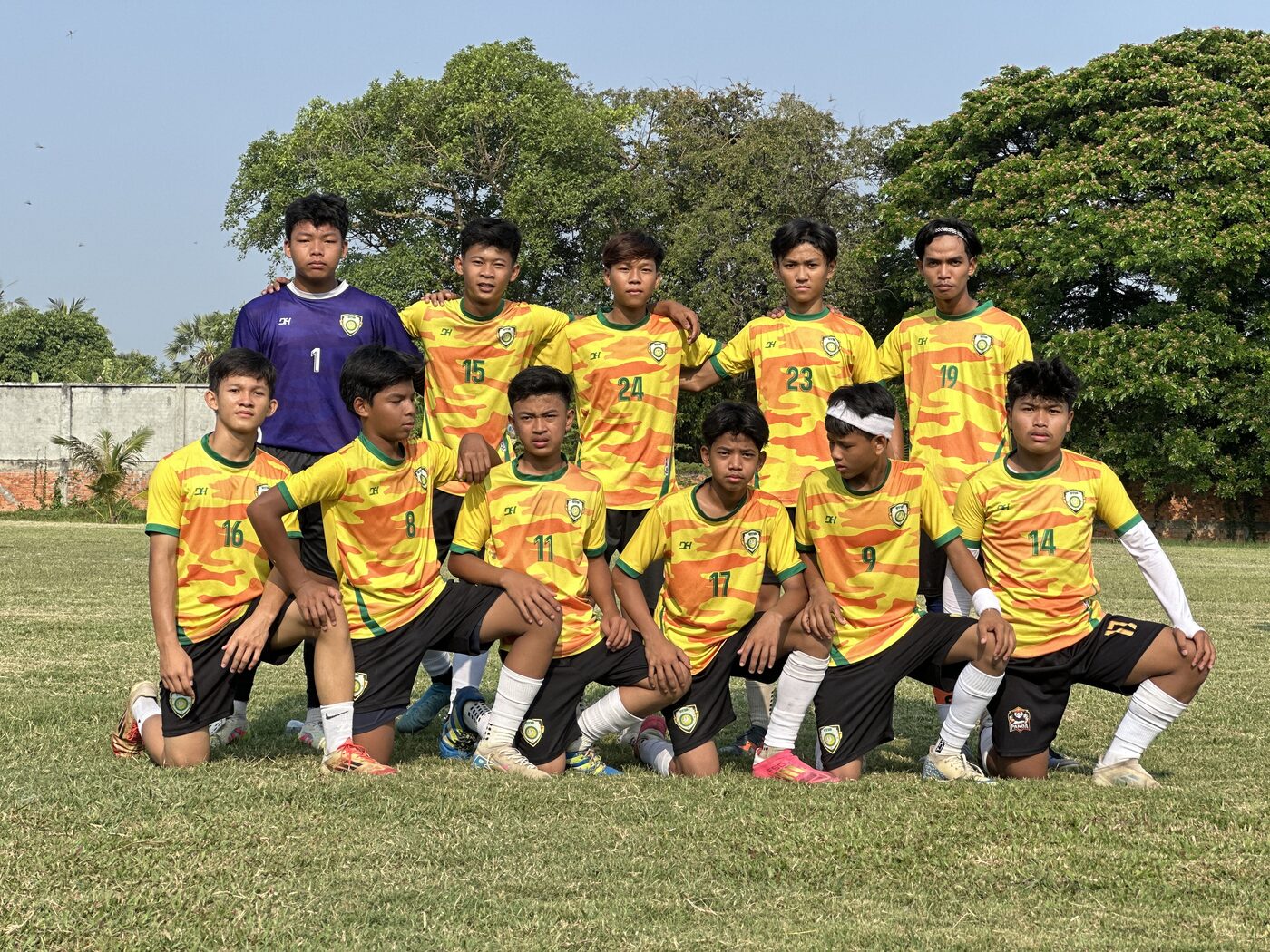 The GTIS football team in yellow and green kit, posed in two rows on the grass pitch
