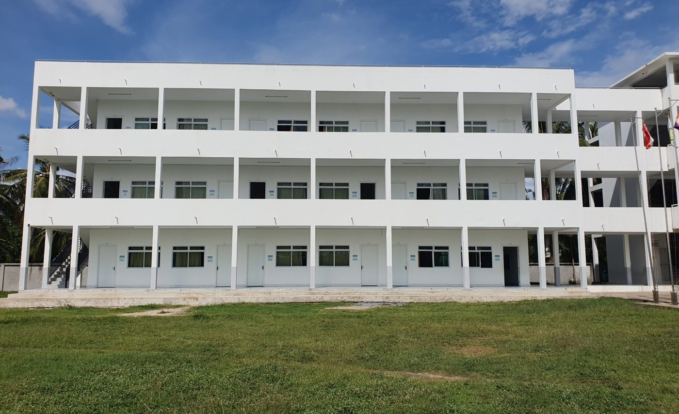 A newly finished three-storey classroom block with open walkways, seen across the school field