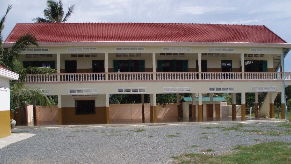 The original two-storey school block, cream and brown with a red tile roof and an open ground floor